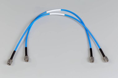 Two blue high-frequency cable adapters with silvery coaxial threaded male connectors on the edges on a gray surface clipart