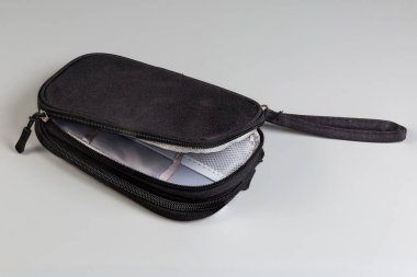 Kısmen küçük siyah tekstil yumuşak erkek çantası, iki fermuarlı ve gri arka planda bilek kayışı şeklinde.