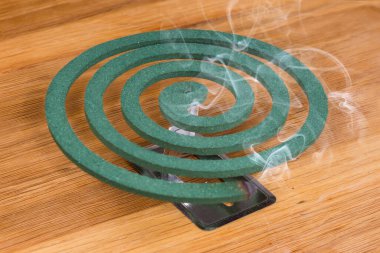 Smoldering fumigating mosquito coil with evaporated of repellent together with the smoke for repel or kill insects outdoors or in well ventilated room, stands on the wooden surface clipart