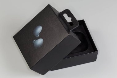 Partly open rectangular black cardboard hang tab packing box for wireless earbuds on a gray surface clipart