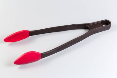 Long handled kitchen locking tongs made with black food grade plastic with red silicone tips on a gray background clipart