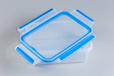 Boş yeniden kullanılabilir şeffaf plastik gıda depolama kabı. Gri arka planda üzerinde bağlanmamış mavi kapağı var.