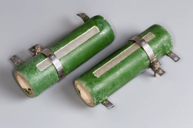 Two old high-power wirewound adjustable resistors on a ceramic core protected with green enamel coating and three tapping points on a gray surface clipart