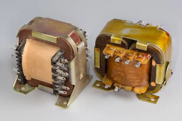 Stock image Two old compact mains shell type transformers for various household or industrial device power supply on a gray surface