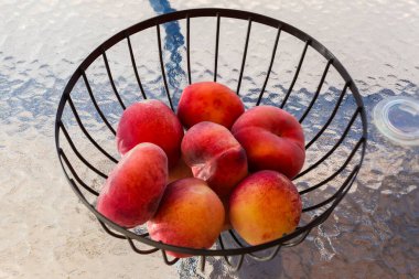 Şeftaliler şekil değiştirir, düz şeftali olarak da bilinir, ya da cam masanın üstündeki metal kafes meyve tabağında incir şeftalileri.