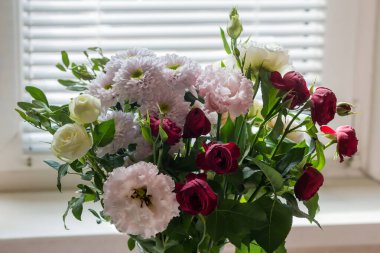 Beyaz ve kırmızı güller buketi, Georginalar ve çiçek vazosundaki diğer çiçekler kapalı arka planda perdeleri açık bir pencere üzerinde.