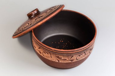 Empty big clay pot decorated with traditional folk ornament used for cooking in an oven with lid pushed aside on a gray background clipart