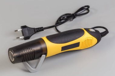Elektrikli sıcak hava tabancası gri bir arka planda duruyor.