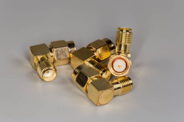Gri bir yüzey üzerinde erkek ve kadın SMA konnektörleri ile birkaç yüksek frekanslı sarı metalik sağ açılı eş eksenli adaptör.