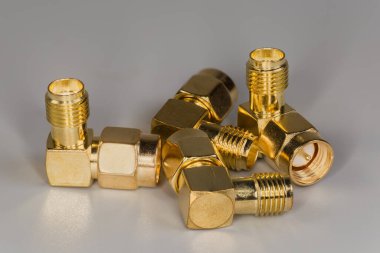 Gri bir yüzey üzerinde erkek ve kadın SMA konnektörleri ile birkaç yüksek frekanslı sarı metalik sağ açılı eş eksenli adaptör.