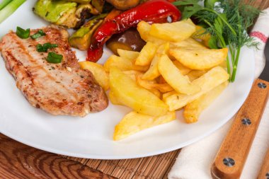 Izgara kemiksiz domuz pirzolası, fırında sebze ve patates kızartması bambu restoranındaki paspasın üzerinde servis ediliyor.