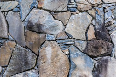 Doğal taşlarla örülmüş engebeli duvarın bir parçası. Bulutlu bir günde farklı şekil ve boyutlarda.