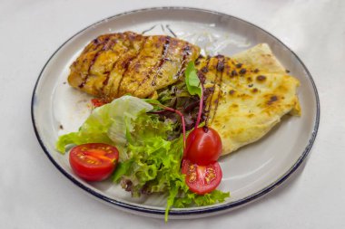 Serving of boneless chicken thigh roasted in batter, known in Italian cuisine as Cosce di pollo with sauce, pita and fresh vegetables on the white dish on a table clipart