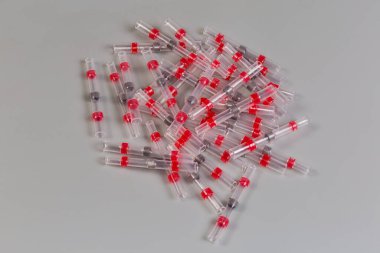 Ortasında lehim halkası olan kırmızı ısı küçültme tüpleri yığını. Eklem için lehim kolları deniyor. Gri bir yüzeyde ısıtarak lehimleme ve yalıtım yapan elektrik kabloları.