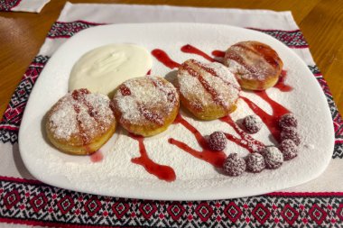 Ahududu reçeli sulandırılmış, üzerine şeker tozu, ekşi krema ve ahududu serpiştirilmiş birkaç kızarmış süzme peynirli krep servis ediliyor.