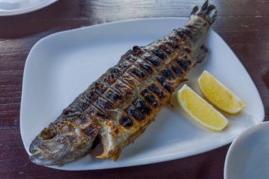 Taze limon dilimleri ile ızgara nehir alabalığı ahşap bir masada, seçici bir odak noktasında yakın plan