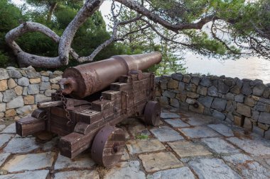 Ortaçağ topları, taş çam ağacının ve diğer Akdeniz bitki örtüsünün arka planındaki antik kalenin kalıntıları üzerine, bulutlu bir sabahta, Bordighera, İtalya,