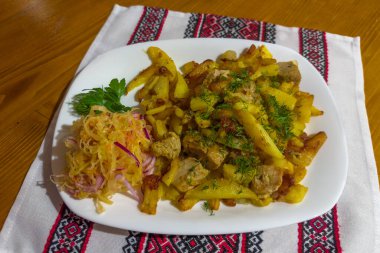 Köy usulü kızarmış patatesler, doğranmış dereotu ve ahşap bir masada salata serpiştirilmiş lahana turşusu ile servis ediliyor.