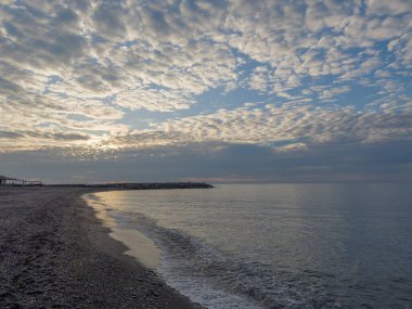 Deniz kıyısının bir kısmı çakıl taşı plajlı. Gökyüzünün arka planında bulutlar bulutlu.
