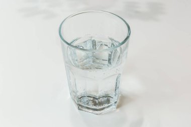 Faceted glass half full with drink water on a white table clipart