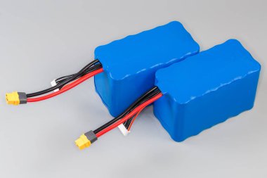 Gri bir arkaplanda UAV ve diğer mobil cihazlar için mavi plastik kaplı güç ve kontrol kablolarına sahip iki şarj edilebilir batarya paketi.