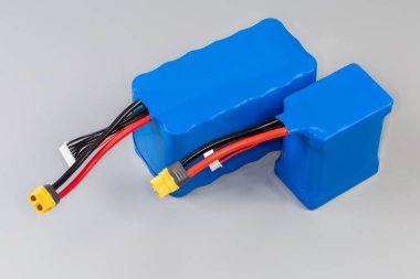 Üzerinde güç ve kontrol kabloları olan iki farklı şarj edilebilir batarya gri bir arka planda UAV ve diğer mobil cihazların güç kaynağı için mavi plastik kaplama