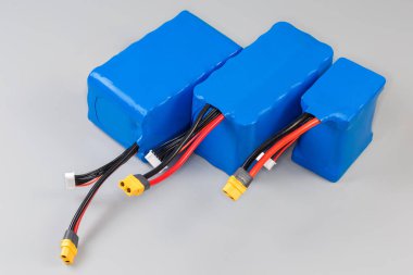 Gri arkaplandaki güç kaynağı ve diğer mobil cihazlar için mavi plastik kaplamalı güç ve kontrol kablolarına sahip farklı şarj edilebilir bataryalar