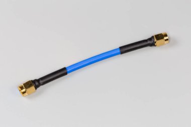 Short blue high-frequency cable adapter with yellow coaxial threaded connectors on the edges on a gray surface clipart