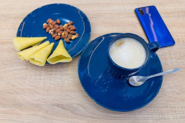 Mavi seramik bardakta kapsül kahve makinesiyle hazırlanmış kahve, peynir ve fındık ile servis edilmiş, ahşap masada kullanılmayan tek porsiyon kahve kapsülleri.