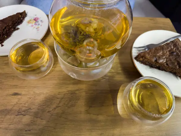 Taze demlenmiş yeşil çay, bitkisel karışım, iki şeffaf cam bardakta, cam çaydanlığa karşı, mum ısıtıcısıyla, masanın üstünde üst görünüm.