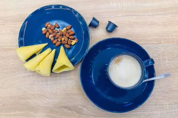 Mavi seramik fındıklı kapsül kahve makinesiyle hazırlanmış kahve, peynir ve fındık ile servis edilmiş, ahşap masada kullanılmayan tek porsiyon kahve kapsülleri, üst manzara.