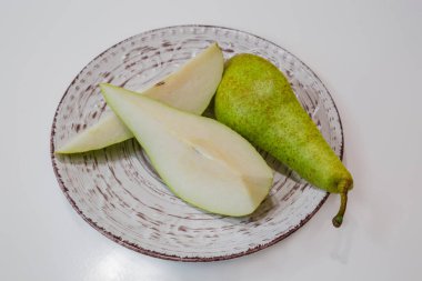 Çeyrek olgunlaşmış yeşil Avrupa armudu beyaz bir masada büyük bir tabakta.