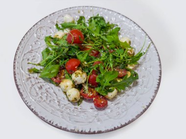 Sebze salatası, mozarella topları, kiraz domatesi, roka ve pesto sosuyla servis edilen beyaz bir masada parmesan peyniri.