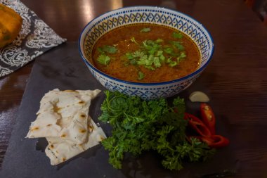 Gürcistan Kharço çorbasının bir kısmı taze doğranmış kişniş ve yeşil, kırmızı biberli, sarımsaklı ve geleneksel düz ekmeklerle servis ediliyor.