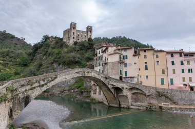 Medieval arched stone bridge over the river against the Old town and  Doria Castle on the hillside at autumn overcast day in Dolceacqua village, Italy clipart