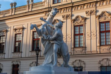 White stone statue of the man fighting with a horse in front of the Upper Belvedere palace in an evening light, Vienna, Austria clipart