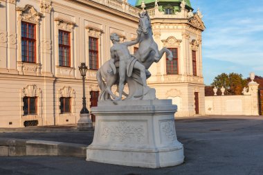 Yukarı Belvedere Sarayı 'nın önünde atıyla savaşan adamın beyaz taş heykeli akşam güneşiyle aydınlanan bir saray cephesinde, Viyana, Avusturya