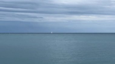 Ufukta deniz suyu yüzeyi ve uzak yelkenli yatı.