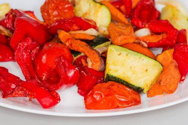 Farklı fırınlanmış sebzelerin karışımı beyaz bir tabakta, ön cephede seçici bir odak noktasında.