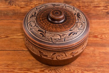 Eski ahşap bir masada, fırında pişirmek için kullanılan geleneksel çiçek süsüsüyle kaplanmış büyük bir kil çömlek.