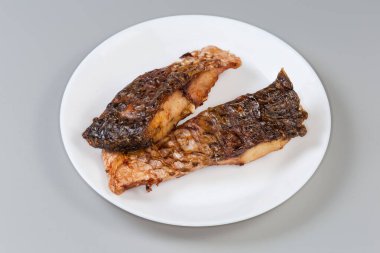 Gri arka planda beyaz tabakta ızgara sazan balığı.