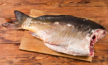 Balık pullarından temizlenmiş büyük, içi oyulmuş bir ayna sazanı ve eski bir kırsal masadaki büyük ahşap kesme tahtasının başı olmadan.