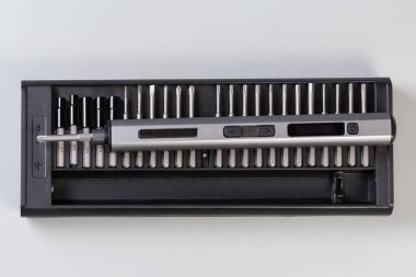 Metal tüp kaplamalı elektirikli şarjlı mini tornavida plastik çantadaki değiştirilebilir parçaların üzerinde gri arka plandaki üst görünümde duruyor.