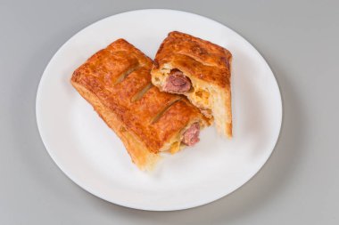 Pişmiş kolay sosis rulosu, hazır sosise sarılmış geleneksel kıyma yerine, gri bir arka planda beyaz bir tabakta ikiye bölünmüş,