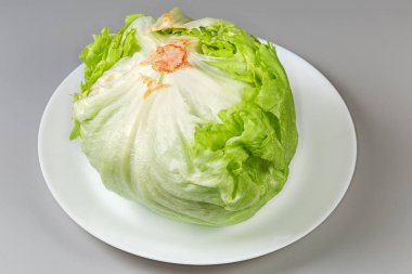 Head of the fresh iceberg lettuce with loosely bunched leaves lies stem up on a white dish on a gray background clipart