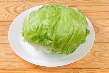 Head of the fresh iceberg lettuce with loosely bunched leaves lies on a white dish on an old wooden rustic table clipart