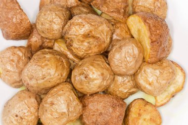 Beyaz bir tabakta, tenlerinde köylü usulü pişirilmiş patates parçaları, seçici bir odak noktasında en üstte.