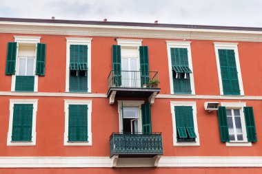 Eski kırmızı binanın üst kısmı. Pencereleri ve balkonları yeşil ahşap dış panjurlarla donatılmış. Yağmurlu bulutlu bir günde.