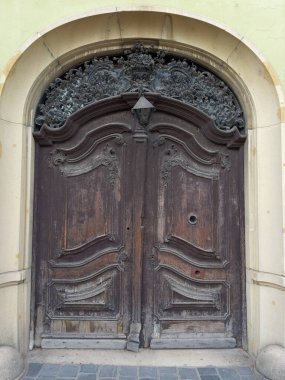 Eski model tahta kaplamalı dış kapı bulutlu bir günde eski bir binanın kemerli geçidinde oyulmuş süs ile karanlığa boyanmış.