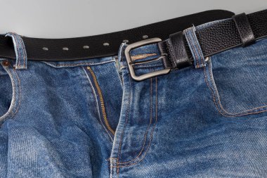 Unfastened black leather belt with conventional buckle with rectangular frame tucked into belt loops of blue jeans, fragment close-up clipart